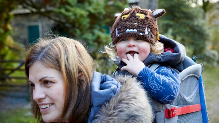 A woman carries a child on her back in the countryside, both are dressed in outdoor winter clothing